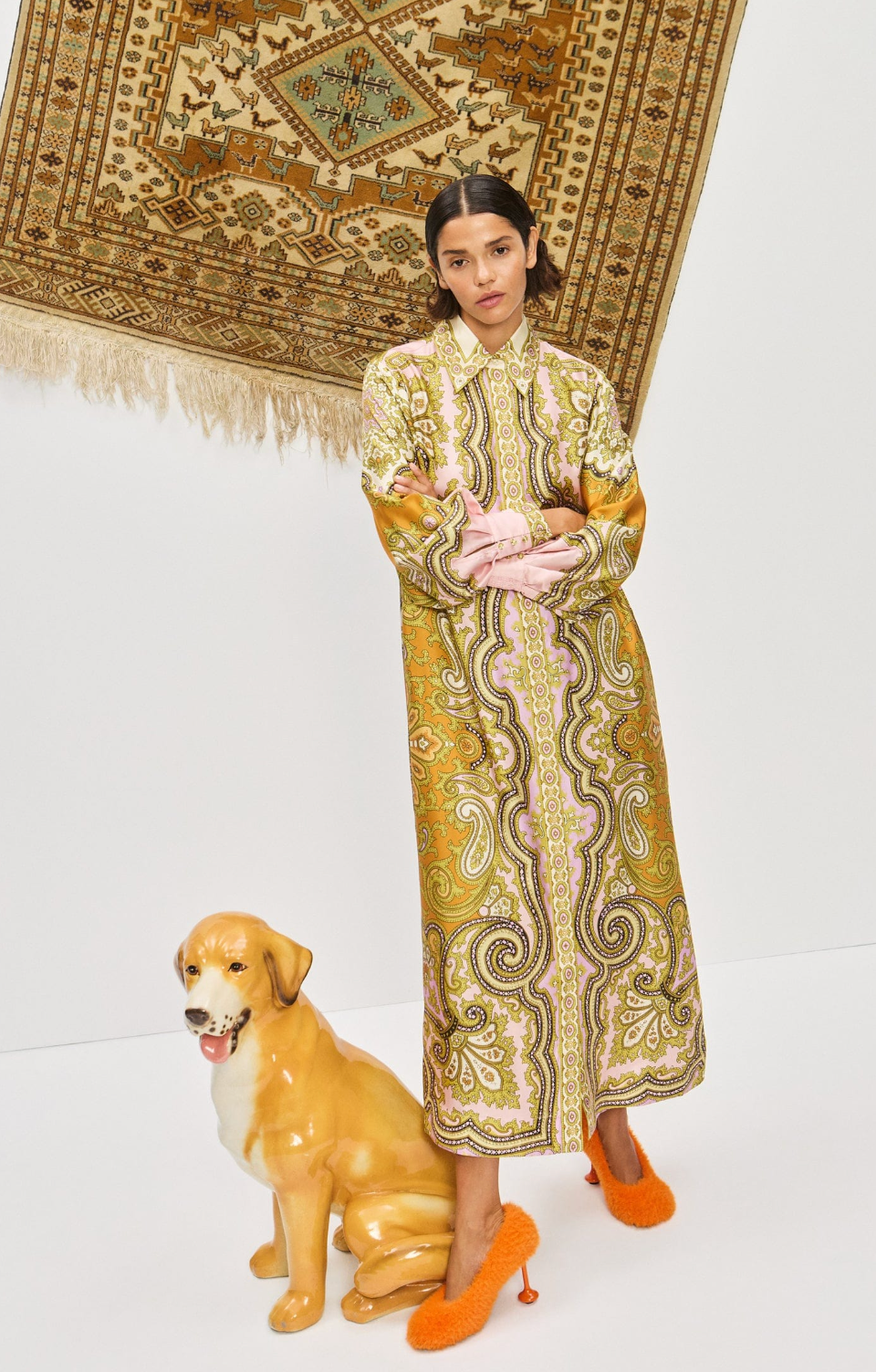 Woman in a patterned dress standing next to a ceramic dog on a white background