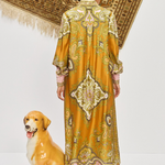 Woman in a patterned dress standing next to a dog statue with a decorative rug in the background