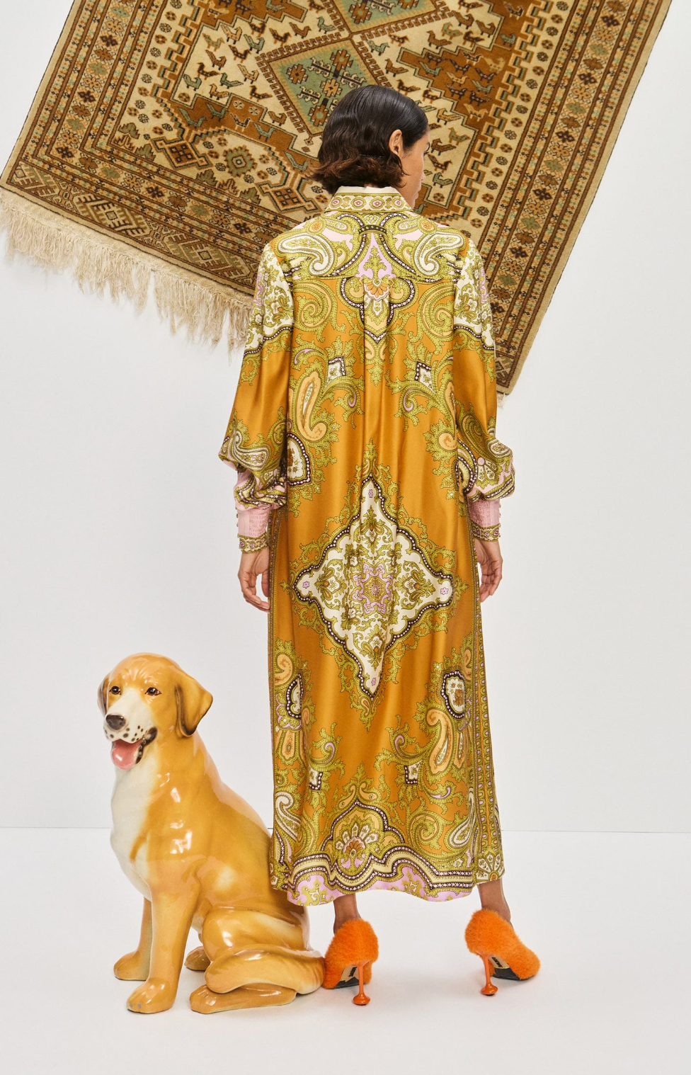 Woman in a patterned dress standing next to a dog statue with a decorative rug in the background