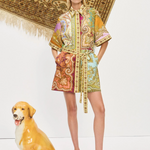 Woman in a patterned dress standing next to a decorative dog statue with a patterned rug in the background.