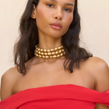 Woman wearing a gold necklace and red off-shoulder top against a beige background
