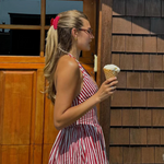 Woman in a red and white striped dress holding an ice cream cone in front of a wooden building.