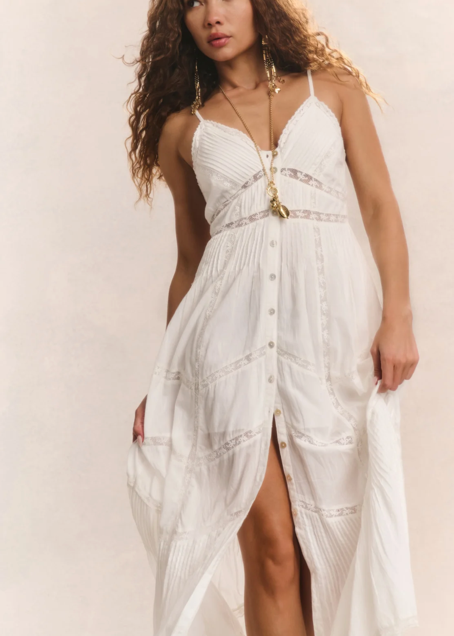 Woman wearing a white dress with gold accents on a plain background