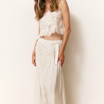 Woman wearing a white lace top and skirt against a white wall