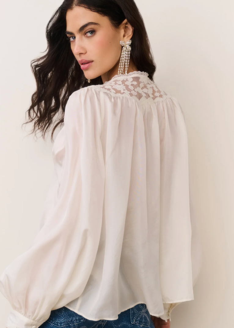 Woman wearing a white blouse with lace details on a plain background