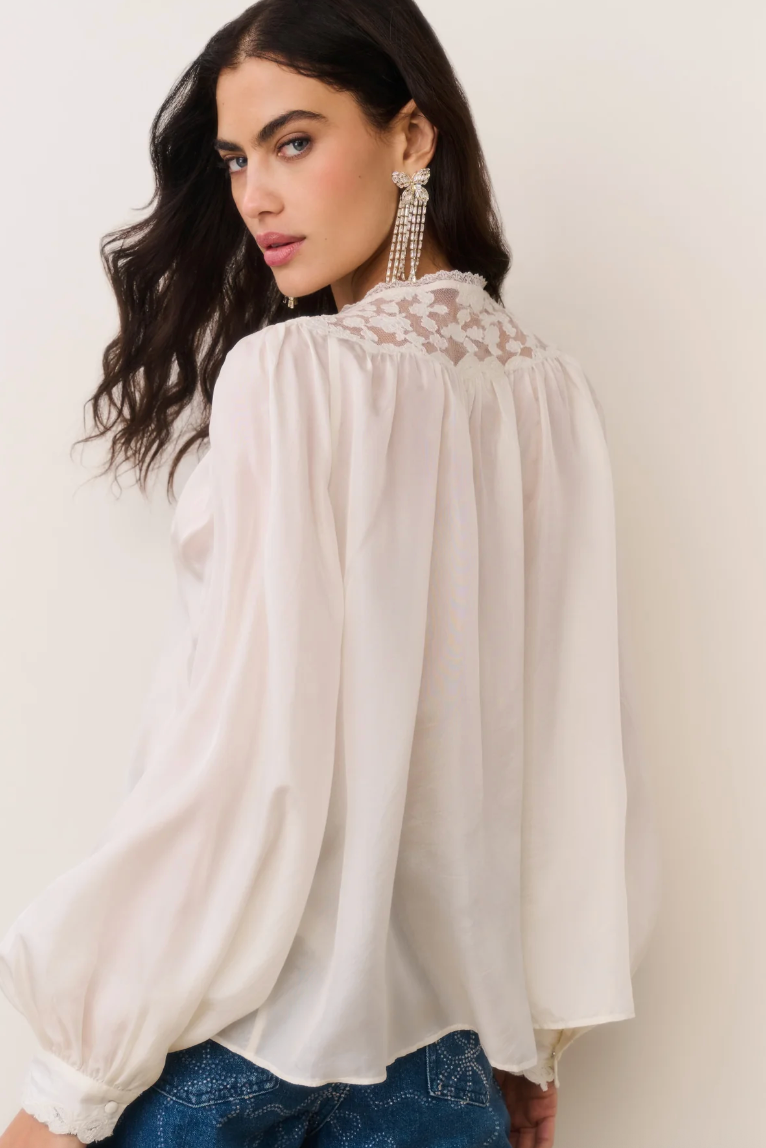 Woman wearing a white blouse with lace details on a plain background