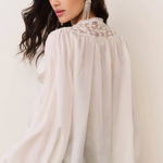 Woman wearing a white blouse with lace details on a plain background