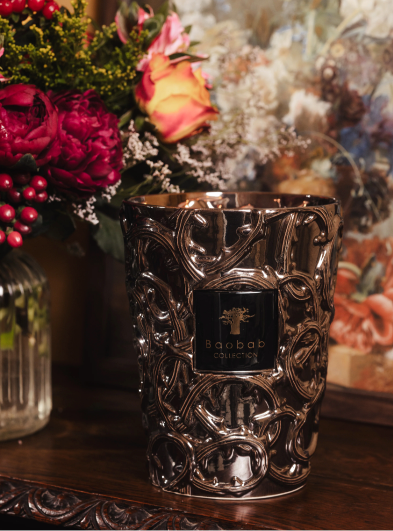 Decorative candle with intricate design on a wooden surface with flowers in the background