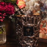Decorative candle with intricate design on a wooden surface with flowers in the background