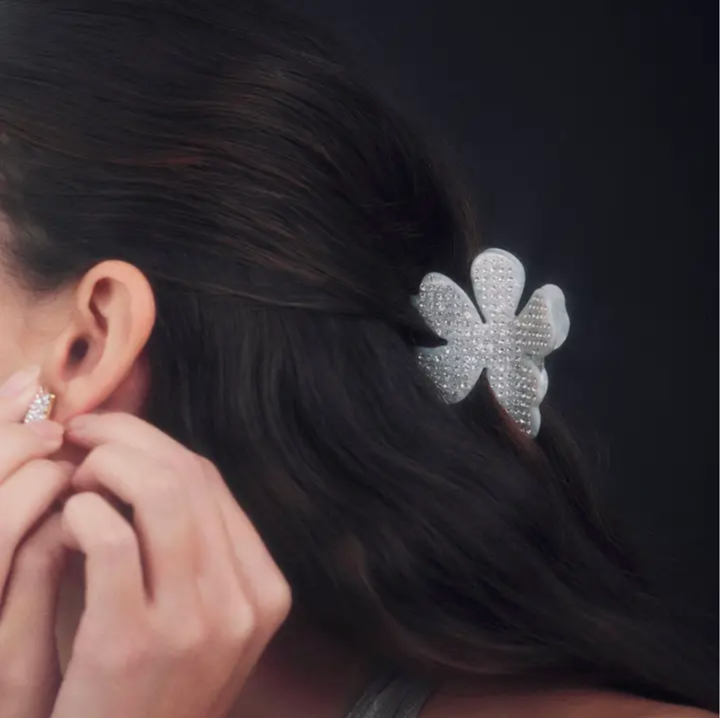 Person wearing a sparkling silver flower shaped hair clip and earring on a dark background