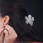 Person wearing a sparkling silver flower shaped hair clip and earring on a dark background