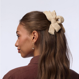 Woman with a beige hair bow in her hair against a light background