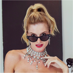 Woman wearing black sunglasses and a large silver necklace against a dark background