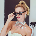 Woman wearing a sparkling necklace and holding black sunglasses, with a blurred background