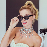 Woman wearing a sparkling necklace and holding black sunglasses, with a blurred background