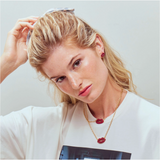 Woman with blonde hair and red earrings wearing a white top with a graphic design.