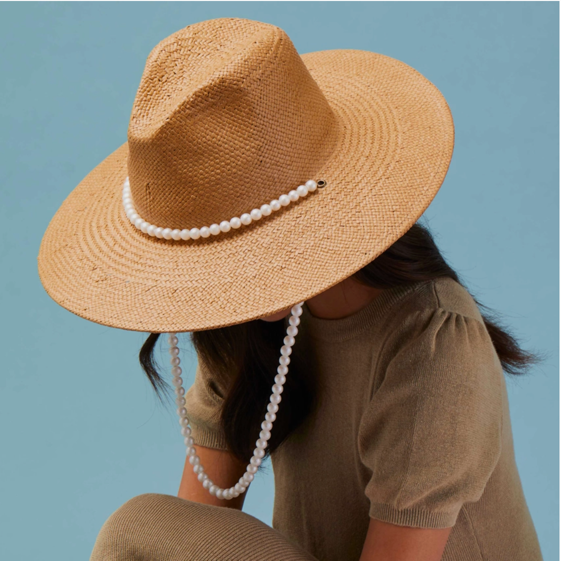 Person wearing a straw hat with a pearl band against a blue background