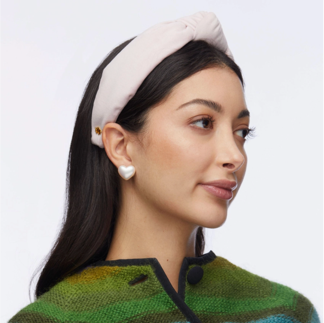 Woman wearing a light headband and green patterned sweater on a plain background