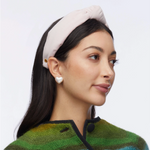 Woman wearing a light headband and green patterned sweater on a plain background