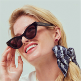 Woman wearing black sunglasses red  lip shaped earrings with a patterned bow in hair against a light background