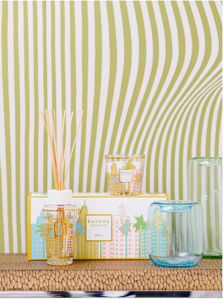 Decorative items including a candle, diffuser, and glass on a textured surface with a striped background