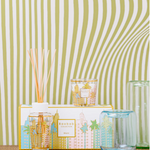 Decorative items including a candle, diffuser, and glass on a textured surface with a striped background