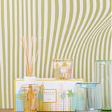 Decorative items including a candle, diffuser, and glass on a textured surface with a striped background