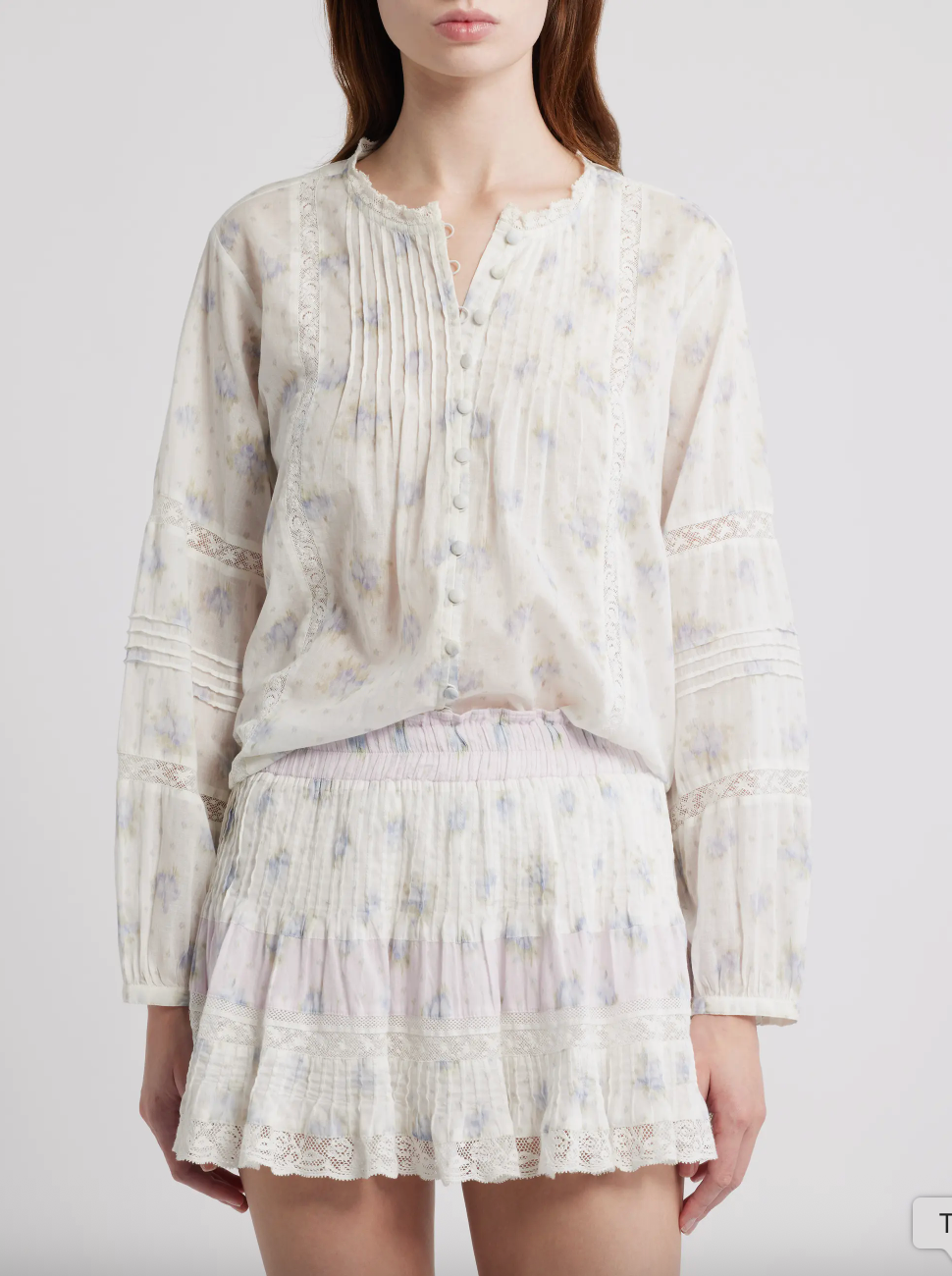 Person wearing a light-colored blouse and skirt with a subtle floral pattern on a plain background