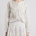 Person wearing a light-colored blouse and skirt with a subtle floral pattern on a plain background