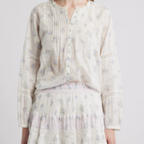 Person wearing a light-colored blouse and skirt with a subtle floral pattern on a plain background