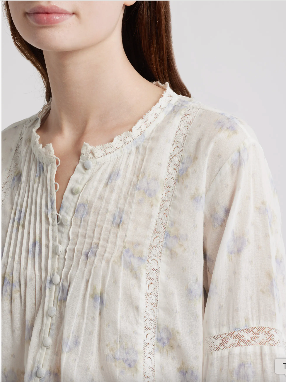 Close-up of a person wearing a light-colored floral blouse with lace details on a plain background