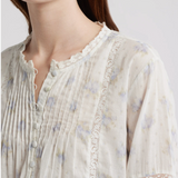 Close-up of a person wearing a light-colored floral blouse with lace details on a plain background