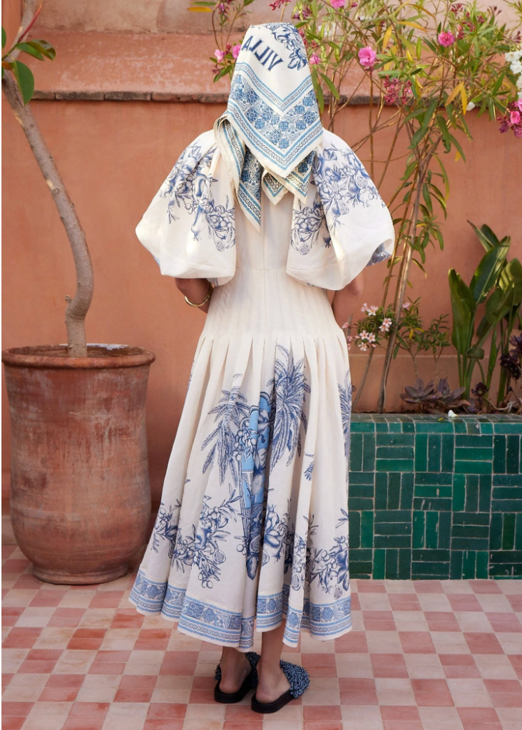 Person wearing a white dress with blue floral patterns in an outdoor setting.