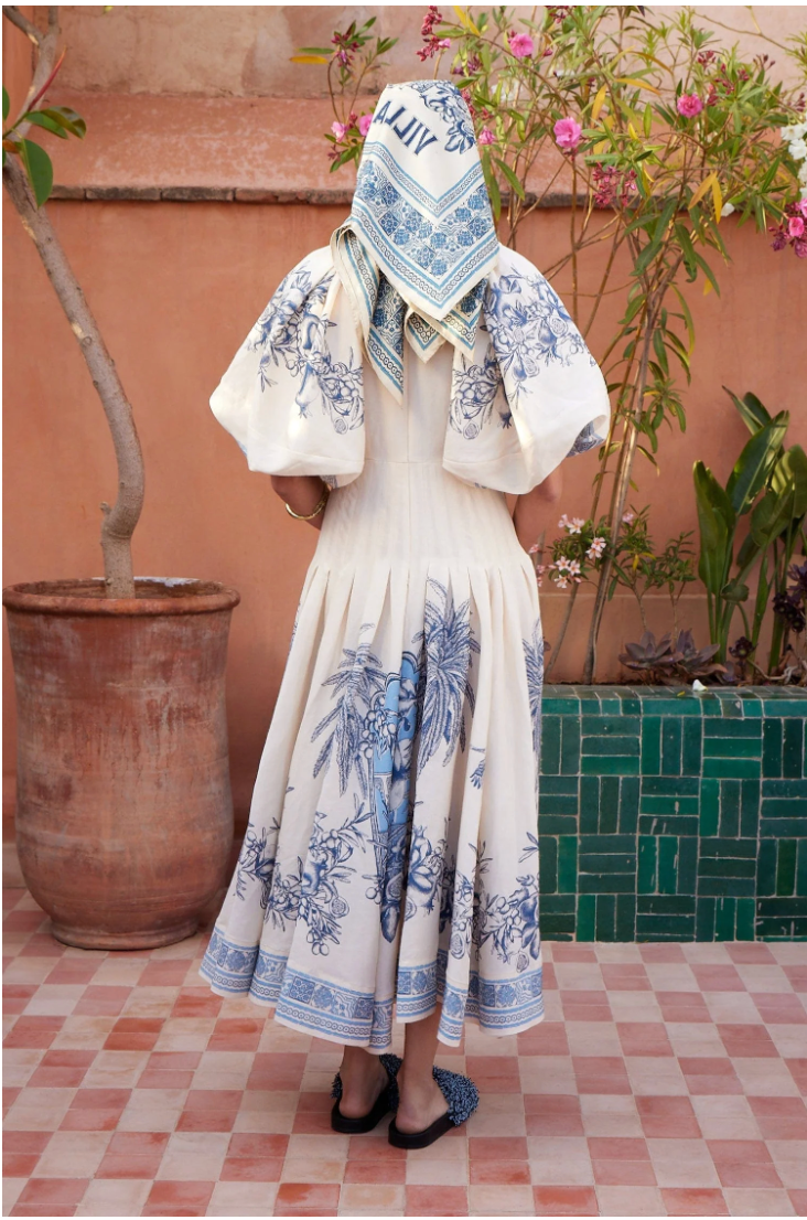 Person wearing a white dress with blue floral patterns in an outdoor setting.
