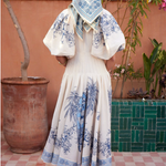 Person wearing a white dress with blue floral patterns in an outdoor setting.