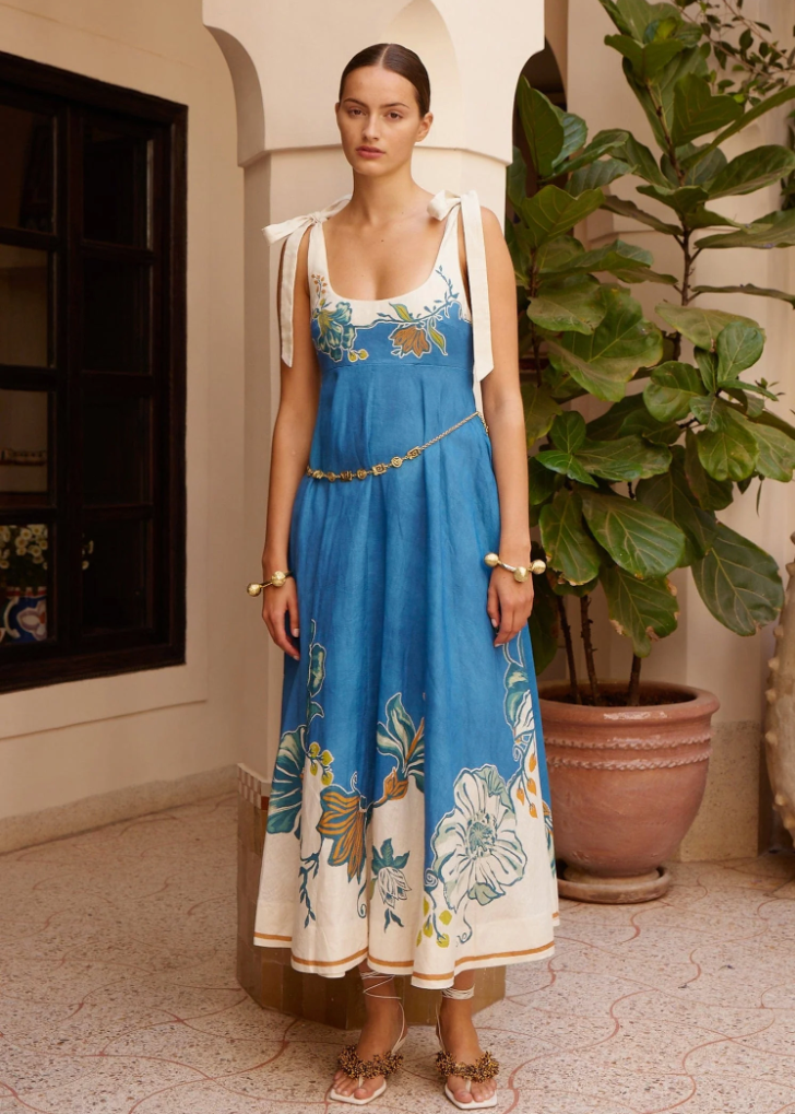 Woman wearing a blue floral dress standing in an indoor setting with plants.
