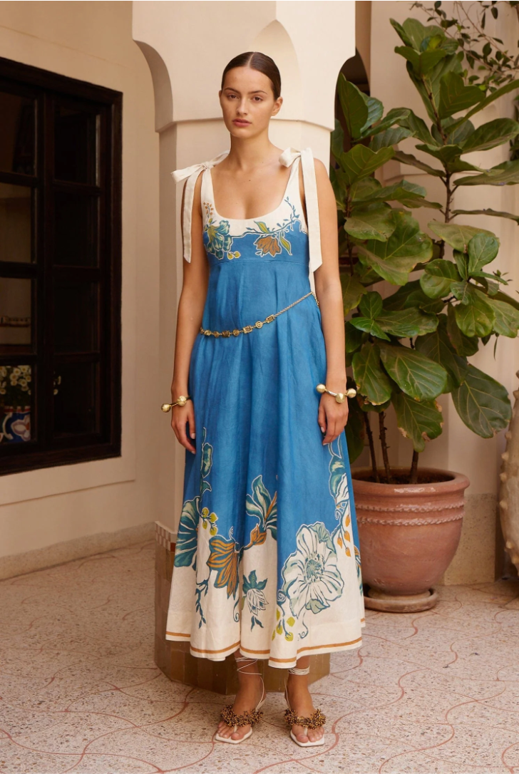 Woman wearing a blue floral dress standing in an indoor setting with plants.