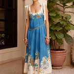 Woman wearing a blue floral dress standing in an indoor setting with plants.