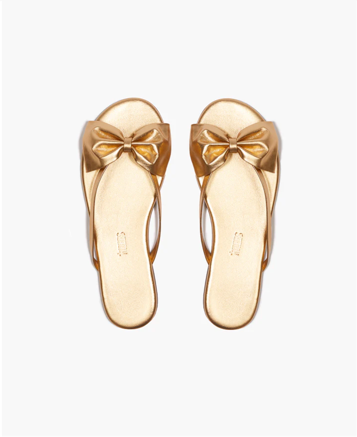 Pair of gold sandals with bow details on a white background