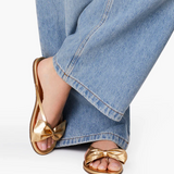 Gold sandals with bow detail worn with blue jeans on a white background