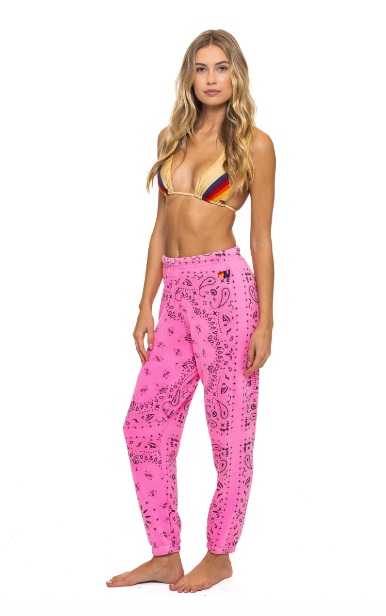 Woman wearing a colorful bikini top and pink patterned pants on a white background