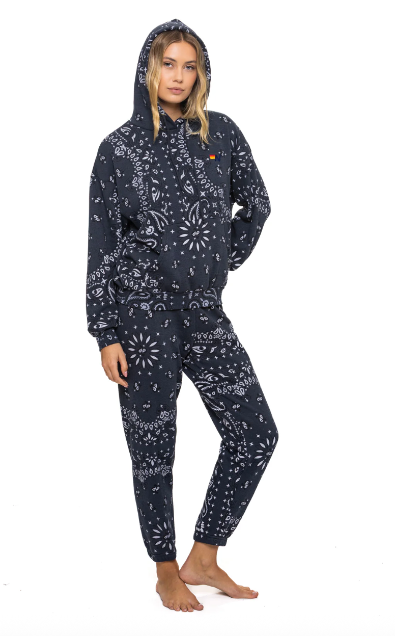 Person wearing a charcoal sweat pants and hoodie with white patterns on a white background 