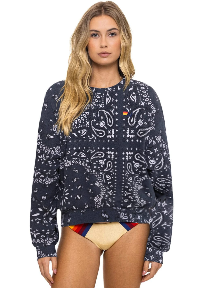 Woman wearing a charcoal patterned sweatshirt with a colorful swimsuit underneath on a white background
