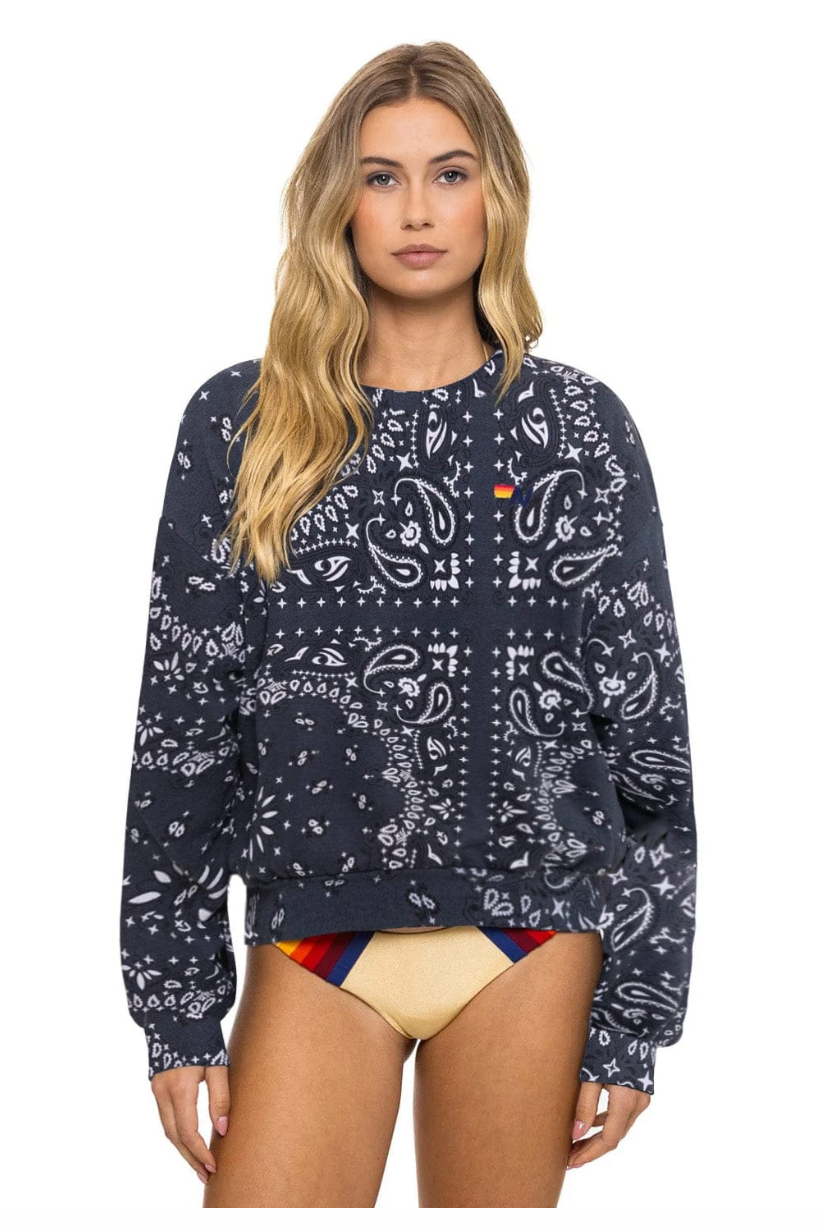 Woman wearing a charcoal patterned sweatshirt with a colorful swimsuit underneath on a white background