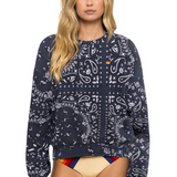 Woman wearing a charcoal patterned sweatshirt with a colorful swimsuit underneath on a white background