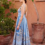 Woman in a blue dress standing in front of a terracotta wall and potted plants.