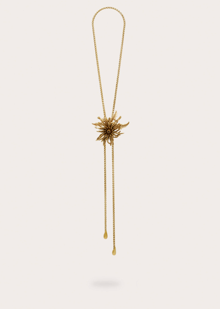 Gold bolo necklace with large flower on a plain background