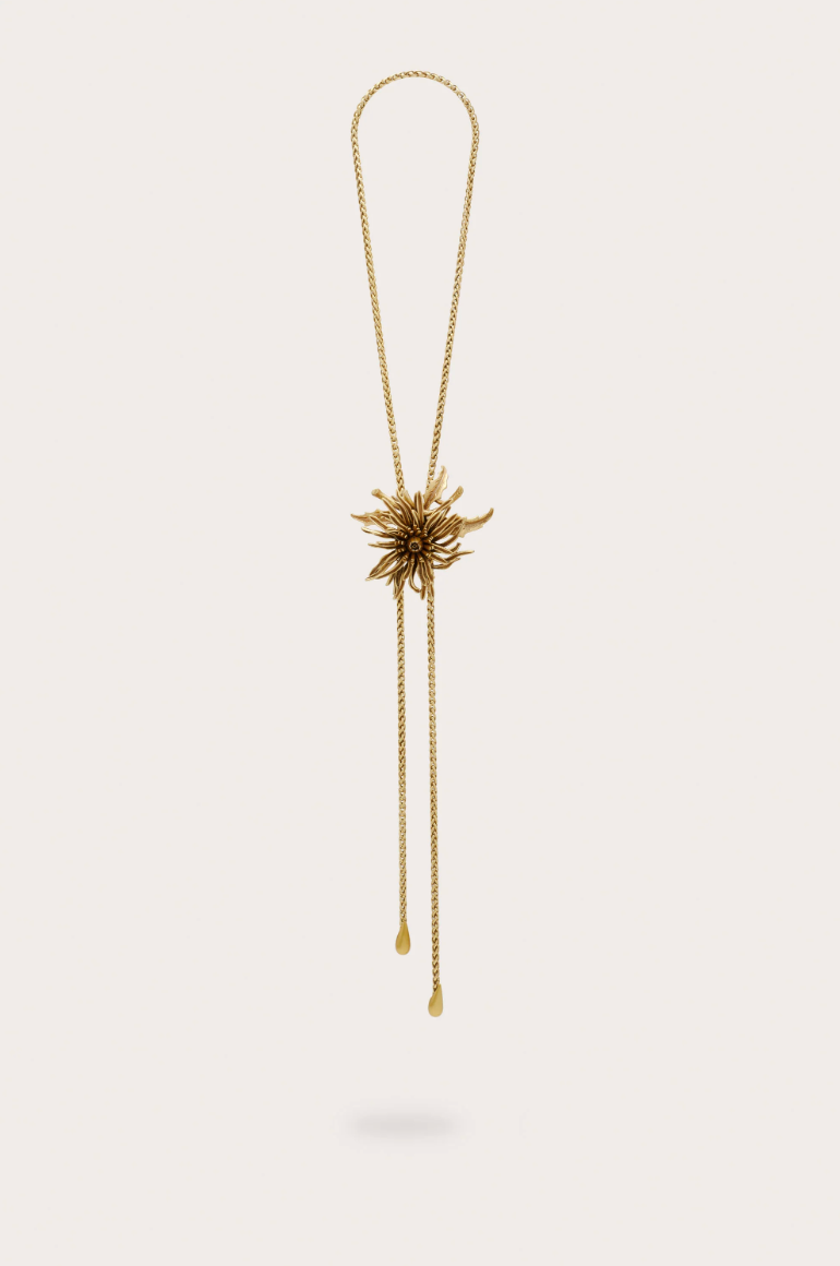 Gold bolo necklace with large flower on a plain background