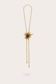 Gold bolo necklace with large flower on a plain background