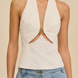 Woman wearing a white halter top with cut-out design and blue jeans on a beige background
